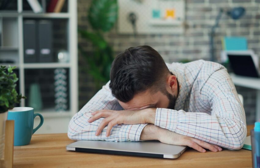 Tired employee at a laptop rubbing her neck, showing signs of workplace burnout