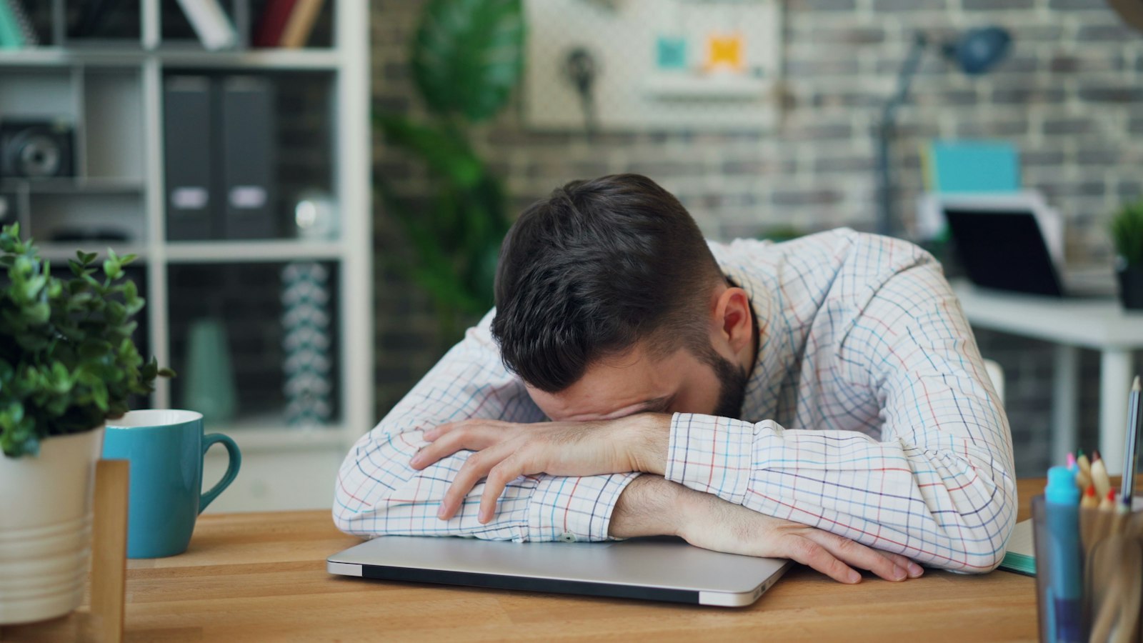 Tired employee at a laptop rubbing her neck, showing signs of workplace burnout