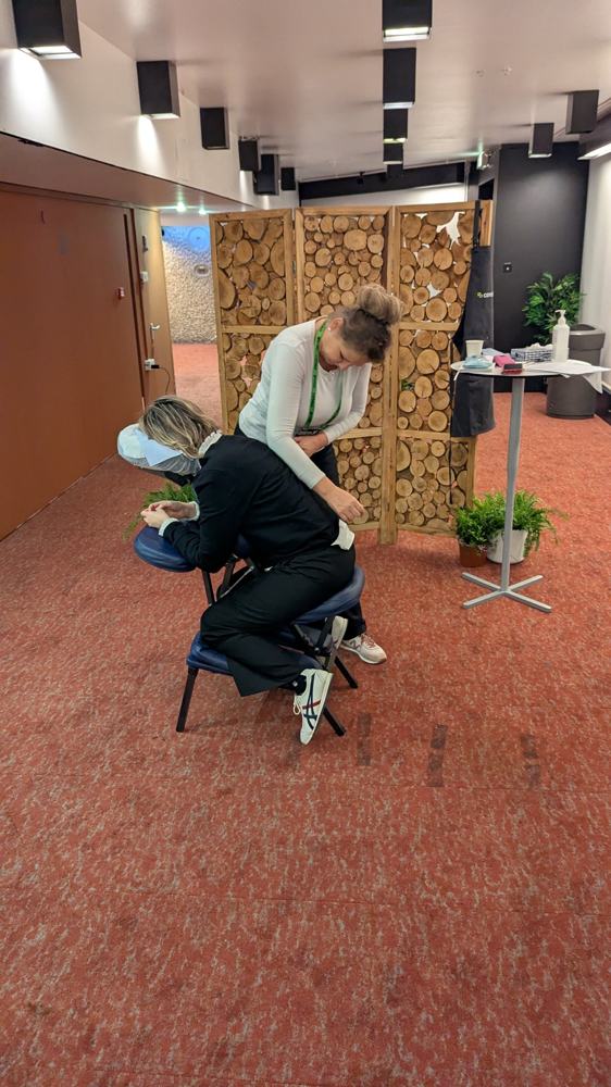 Chair massage station with a wooden screen and plants at a corporate event
